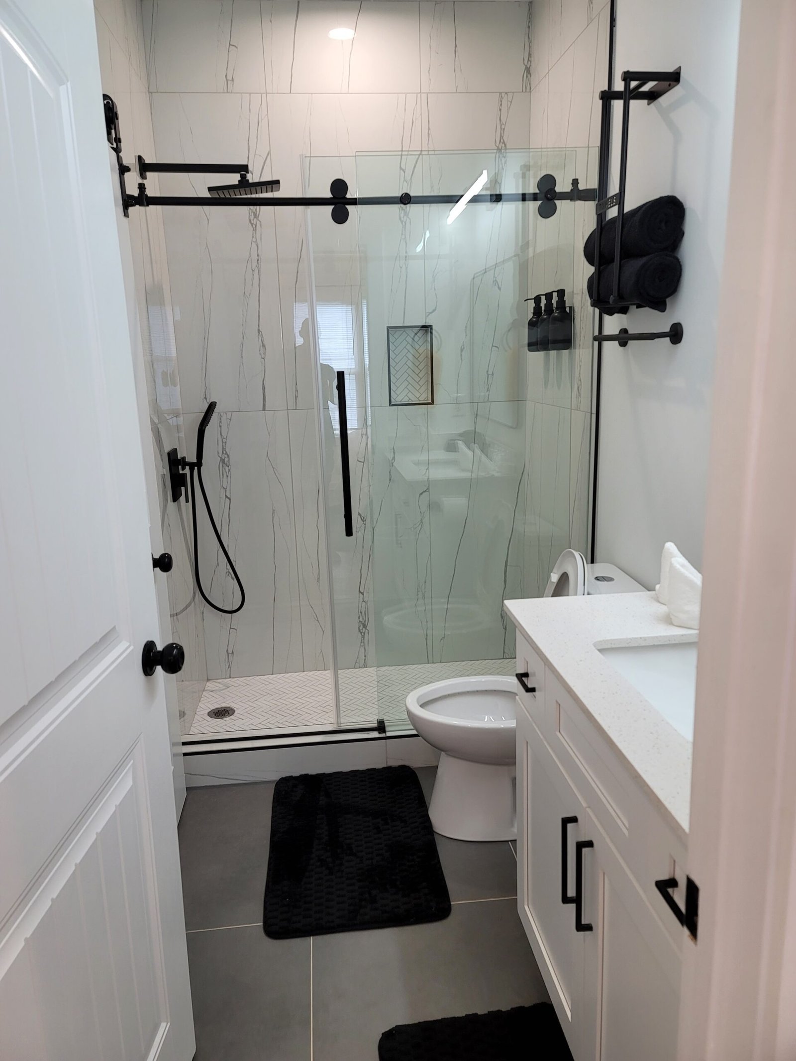 Home 3 Modern bathroom remodel by Above All Handyman featuring frameless glass shower with matte black fixtures, white vanity with quartz top, and large floor tiles – 1498 Murphy Ave, Atlanta, GA.
